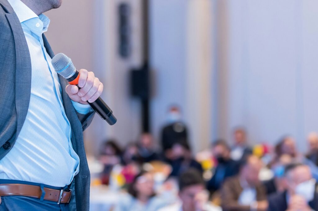 A businessman public speaking with a microphone in front of an audience at a business conference